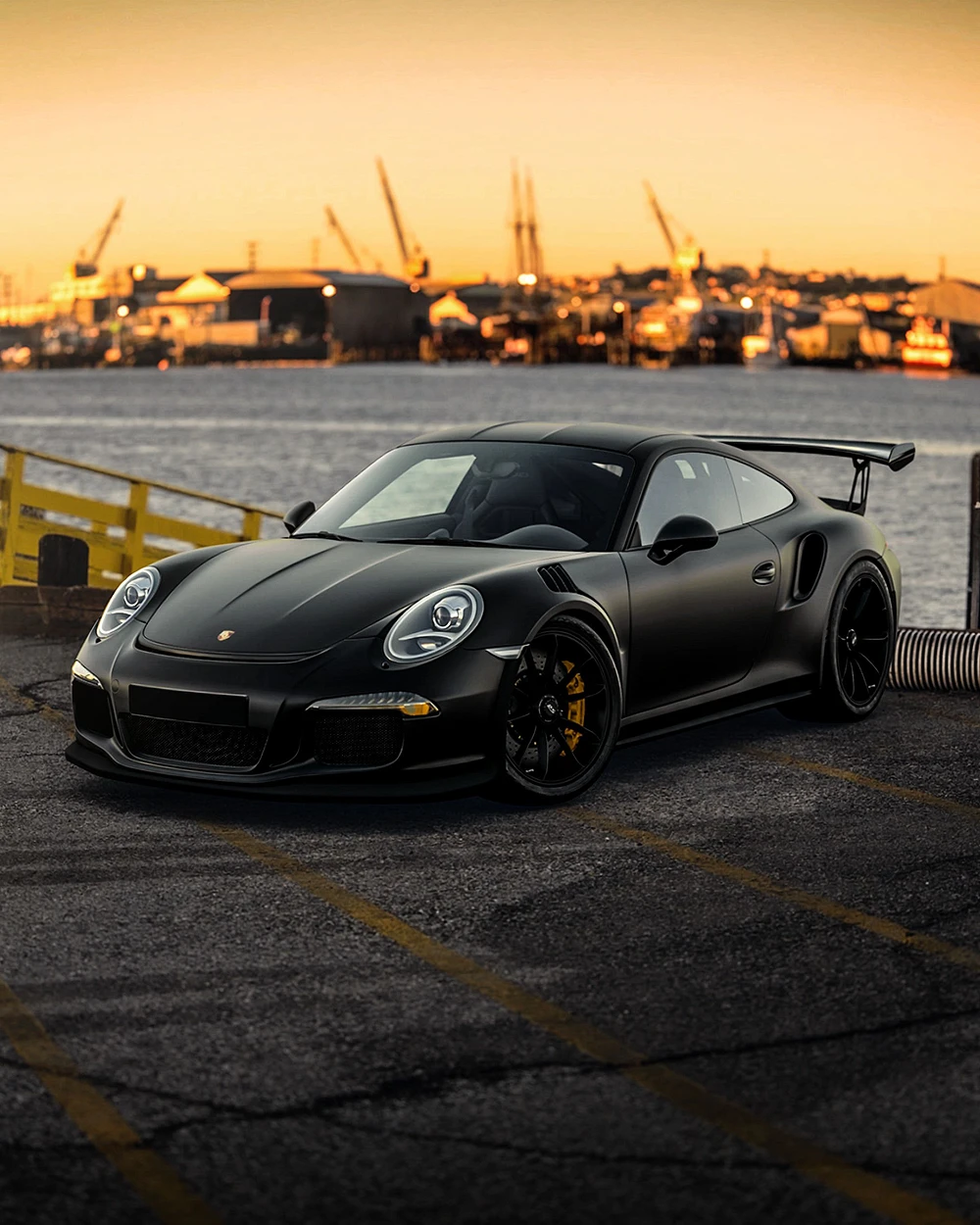 Porsche 911 GT3RS noire matte au coucher du soleil dans une zone industrielle